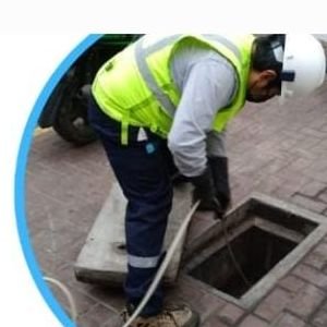 Técnico de MPU realizando limpieza de alcantarillado en un registro de la vía pública