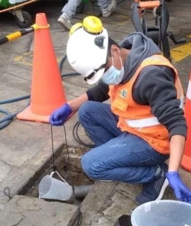 Técnico de MPU tomando muestra de aguas residuales en la vía pública